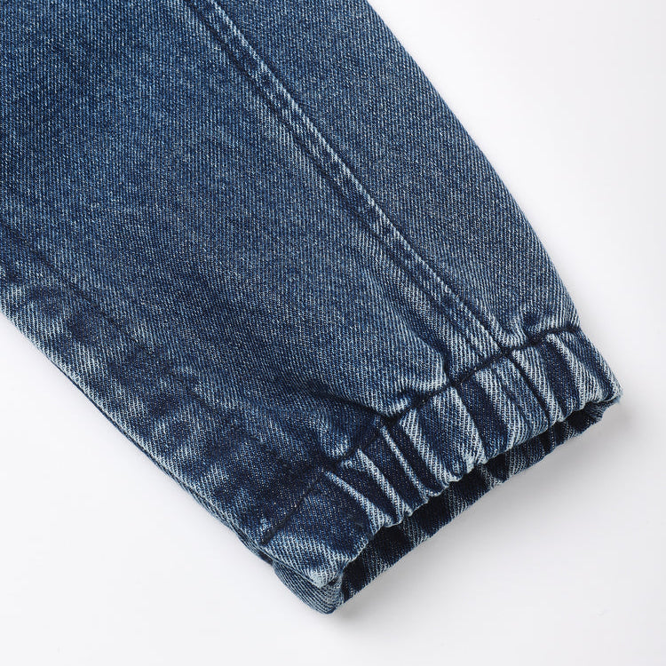 Close-up of a dark blue denim garment cuff with an elastic gathered hem, shown on a plain white background.