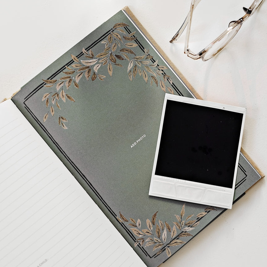 Green notebook with floral design on cover, white photo frame, and glasses on a light surface