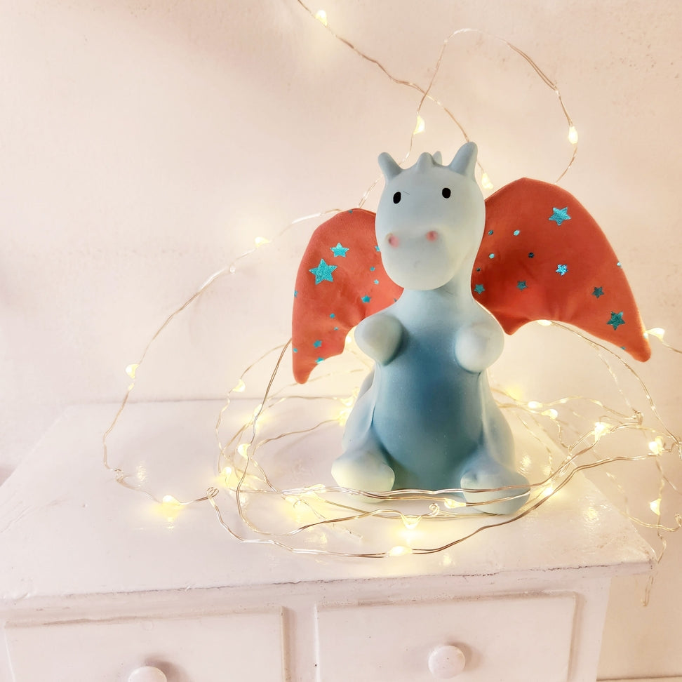 Decorative figurine of a blue creature with red wings on a white surface with string lights.