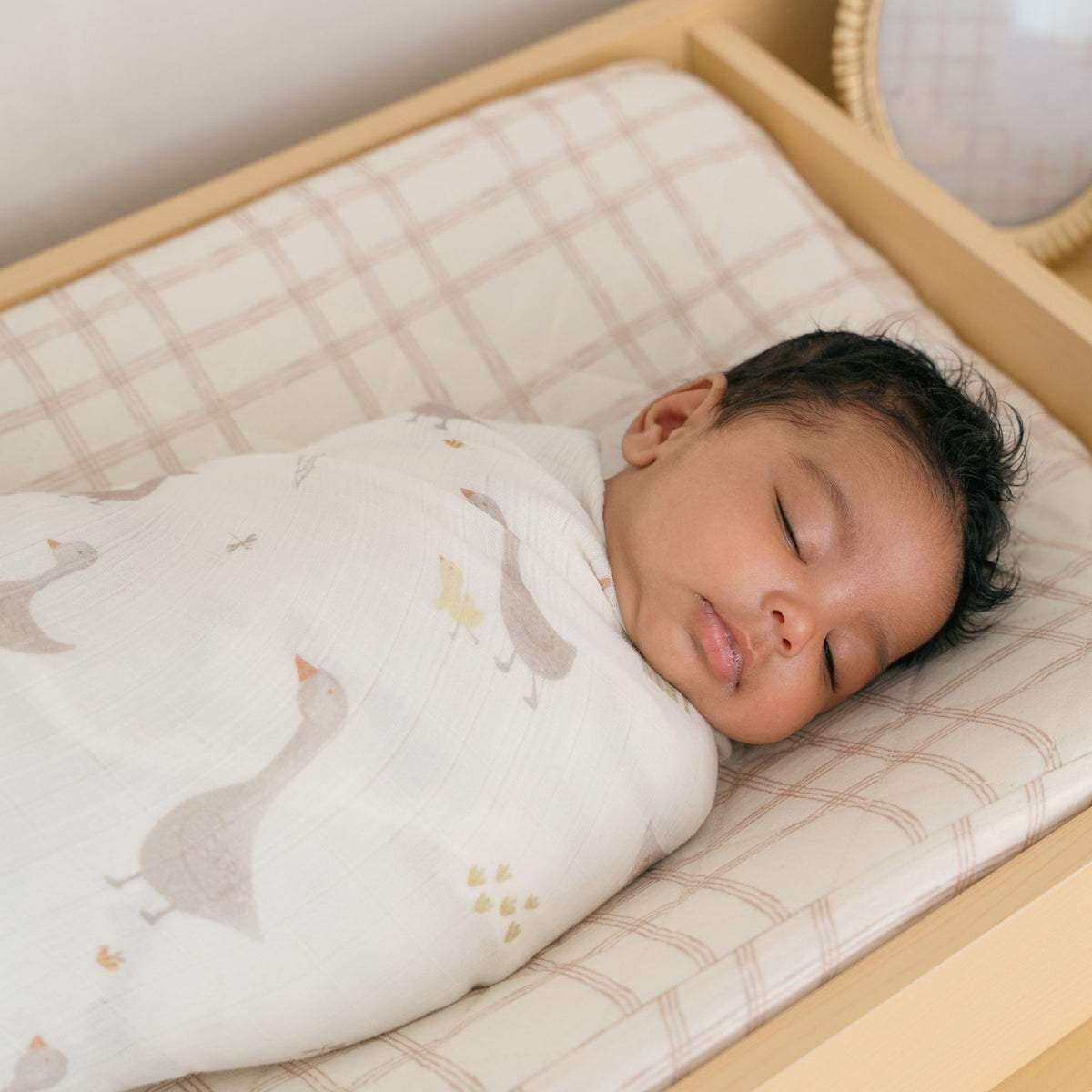 Baby sleeping in a crib with a swaddle blanket featuring animal patterns.
