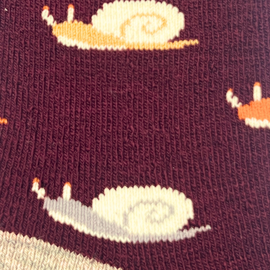 Close-up of a knit fabric with a burgundy background and a repeating snail pattern in cream, light gray, and orange.