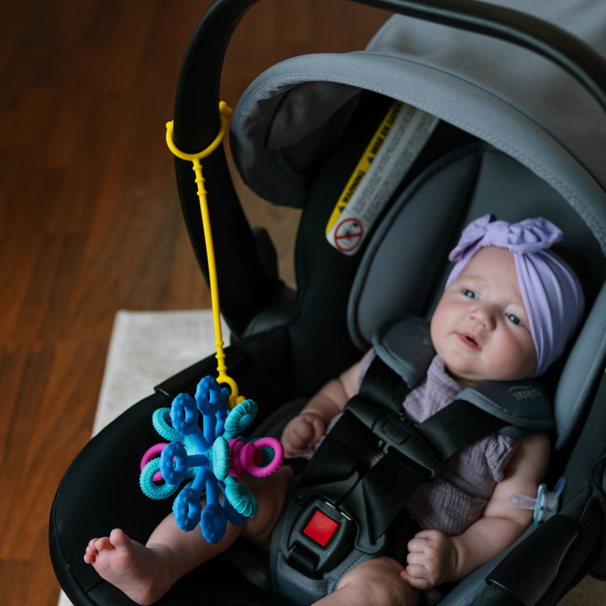 Baby in a car seat with a colorful toy hanging from it