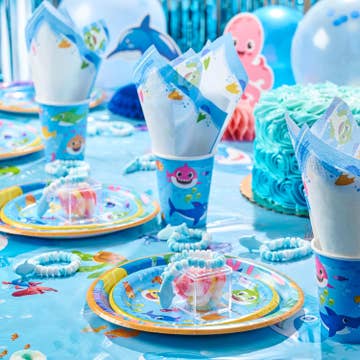 Children's party table setting with ocean-themed cups, plates, and cake.