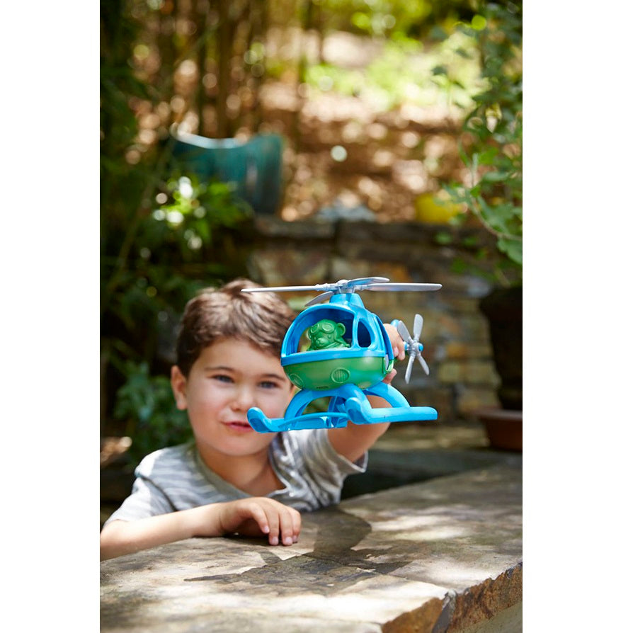 Child holding a toy helicopter outdoors with greenery in the background
