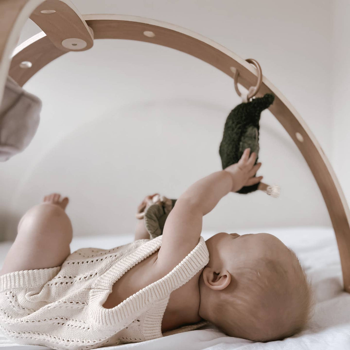 Baby playing with a hanging toy on a white blanket