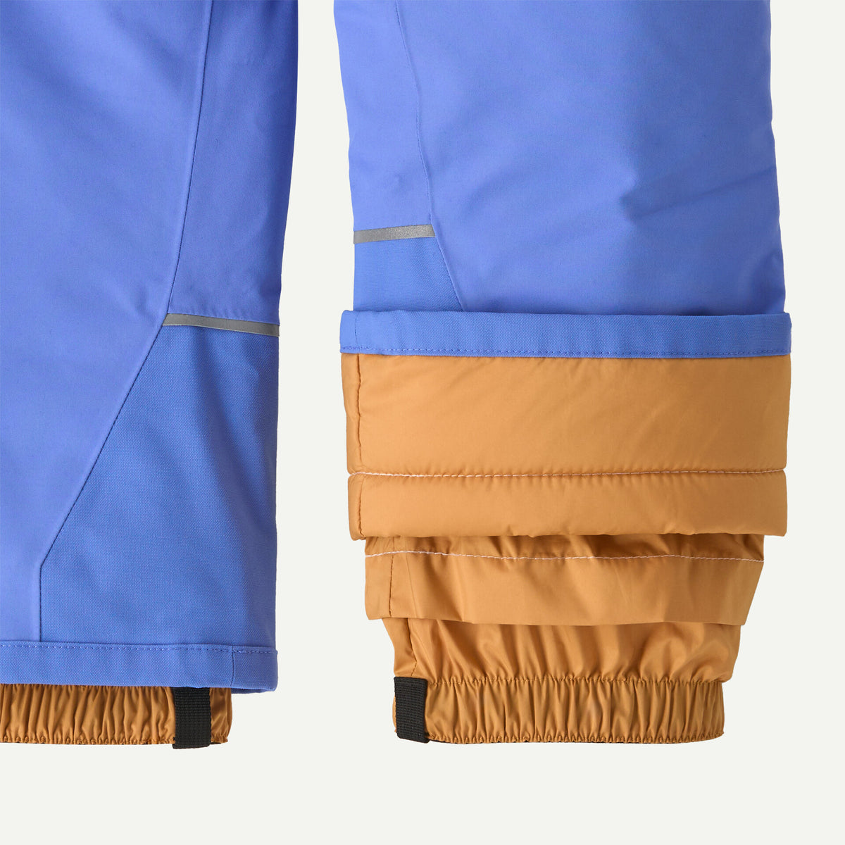 Close-up of a pair of blue and tan insulated pants showing the cuff details, including reflective striping and elasticated openings.