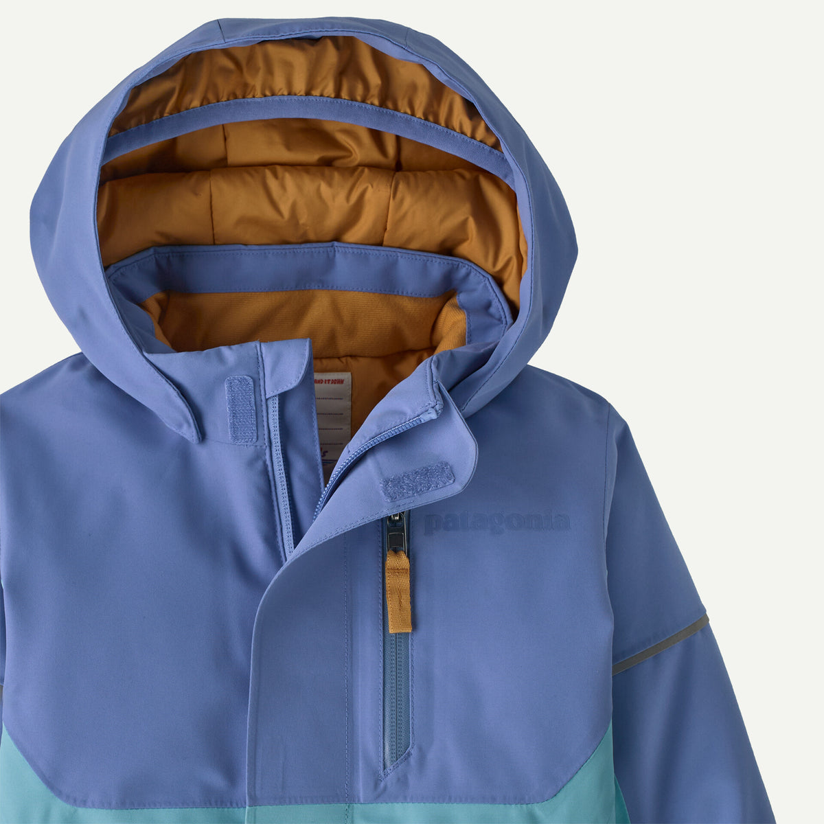 Close-up of a Patagonia hooded jacket in dusty blue with a tan interior lining and a light aqua lower panel, shown against a plain light background.