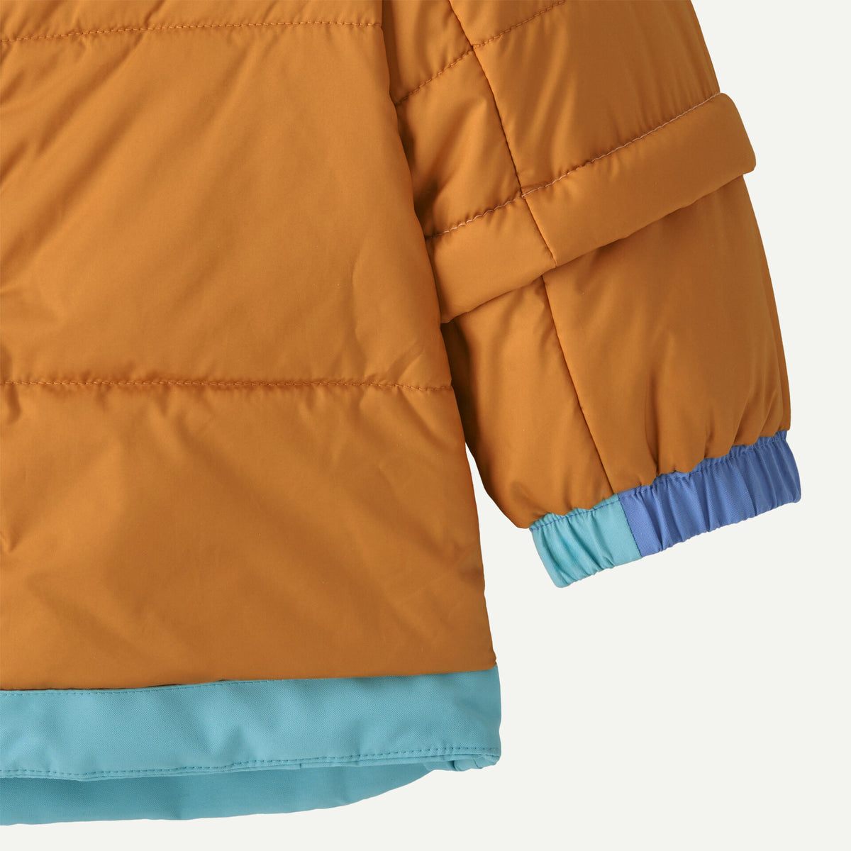 Close-up of a quilted mustard-orange puffer jacket sleeve with elastic cuffs in light blue and medium blue, plus a matching light blue hem.