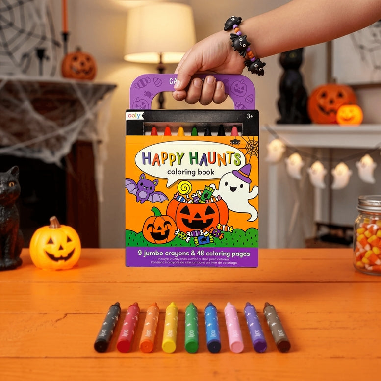 Happy Haunts coloring book with crayons on a table in a Halloween-themed room.