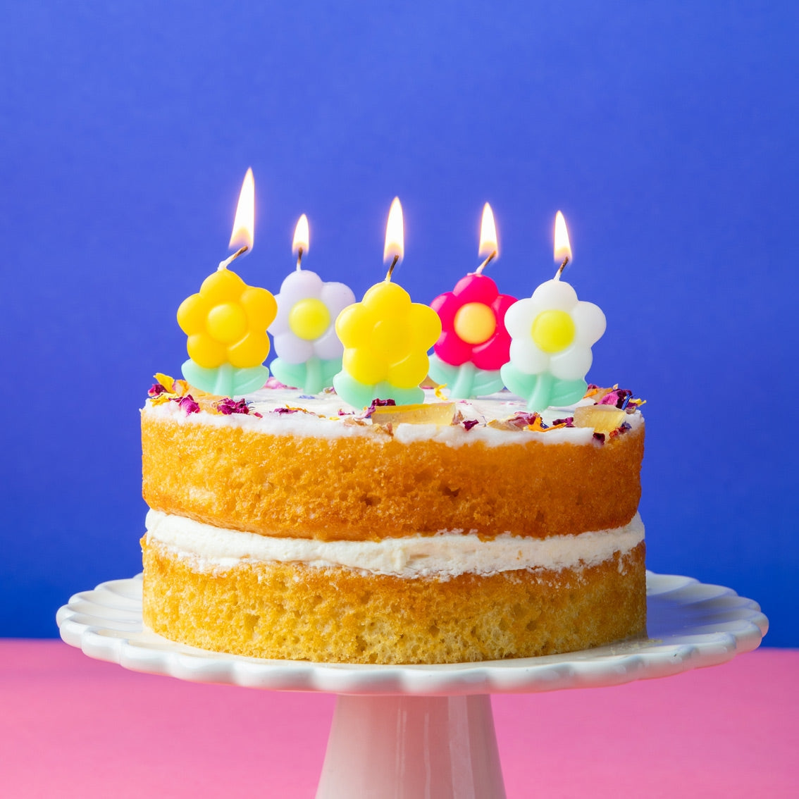 Two-layer cake with flower-shaped candles on a pink and blue background
