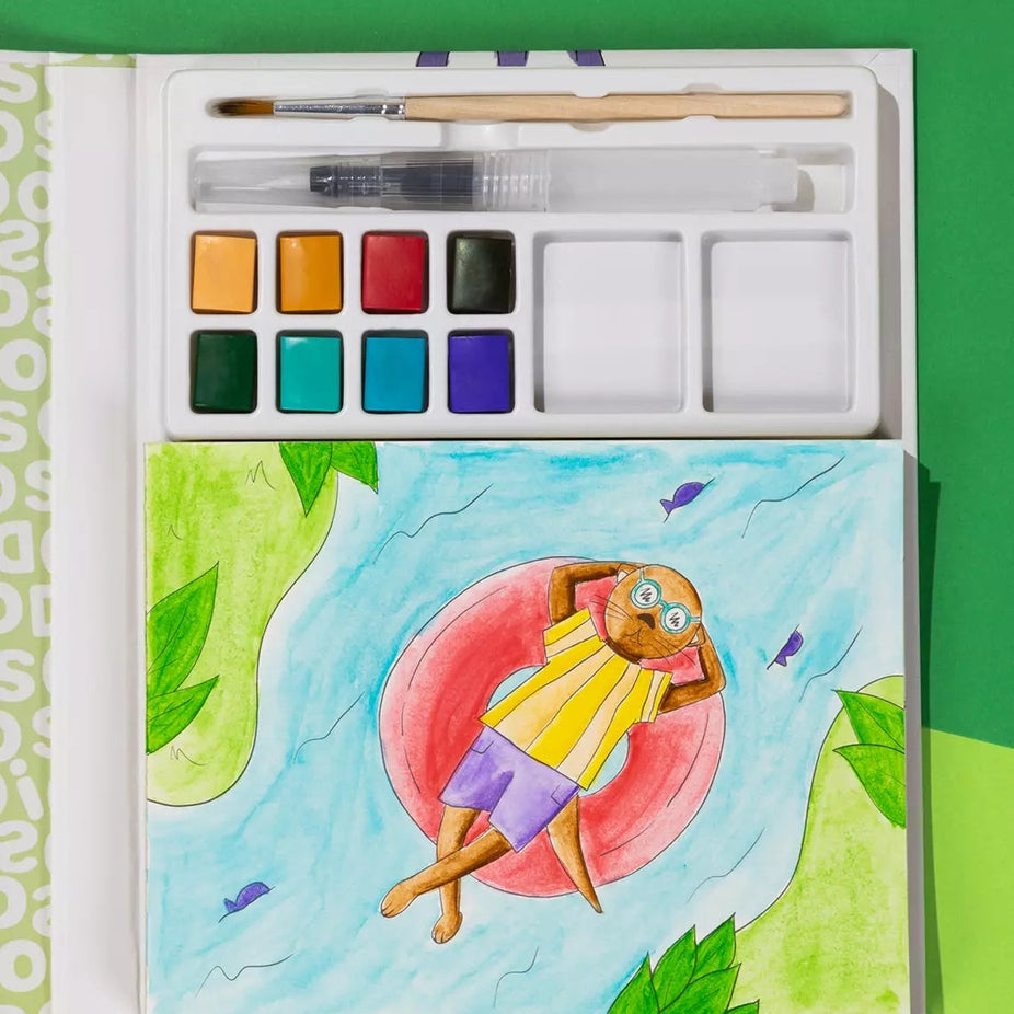 An open watercolor painting book or palette set on a bright green background. The top section contains a paintbrush, paint wells, and a palette of watercolor colors.