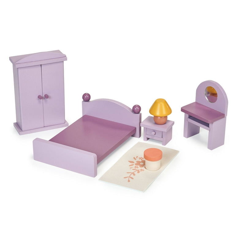 A product photo of the Wooden Bedroom Furniture set by Mentari, featuring a collection of miniature purple wooden dollhouse furniture arranged on a white background. The set includes a double bed with a purple frame and bedding, a wardrobe with opening doors, a dressing table with a matching stool, a bedside table topped with a yellow-shaded lamp, and a small printed rug with a floral pattern.