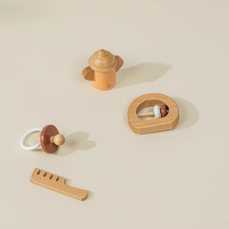 A set of wooden baby toys arranged on a warm beige background, including a small bottle-shaped rattle, a pacifier, a comb, and a circular toy with beads.