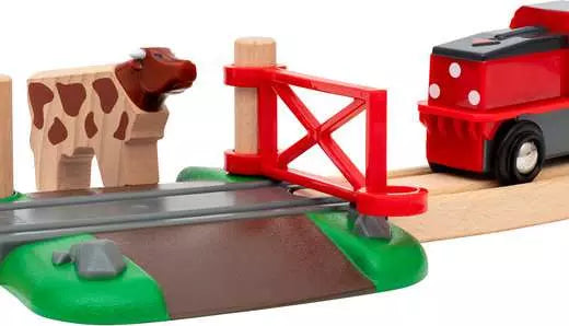 Toy train set with wooden track, cow figure, and red gate on a wooden platform.