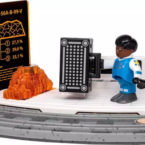 A toy construction vehicle scene with a blue and white minifigure standing beside a black control panel, an orange translucent rock, and a black display screen showing statistics, all on a white and gray vehicle base against a white background.