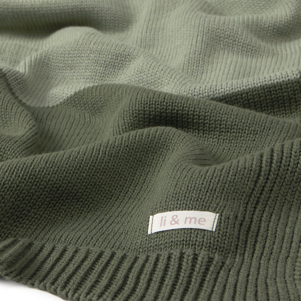 Close-up of a ribbed knit garment in an olive green color, showing the texture and a small white label with the brand name 'li & me'.