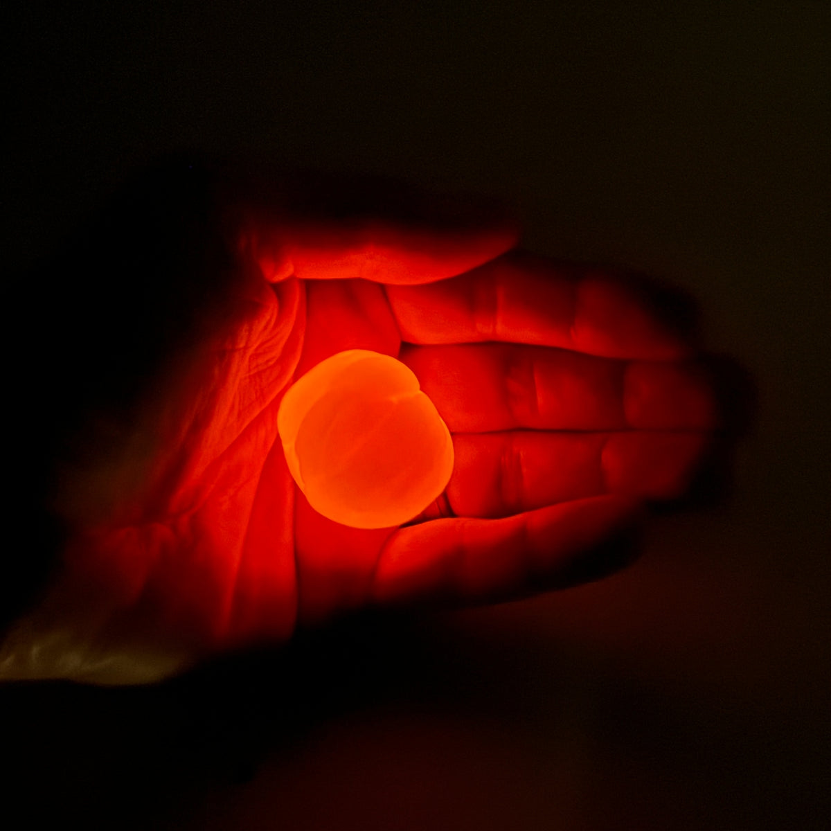 A glowing orange-red circular light or orb held in an open hand against a dark background.