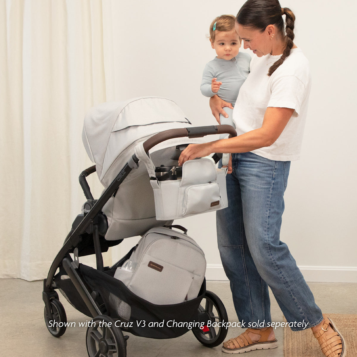 Woman adjusting a stroller with a child standing next to it in a home setting.