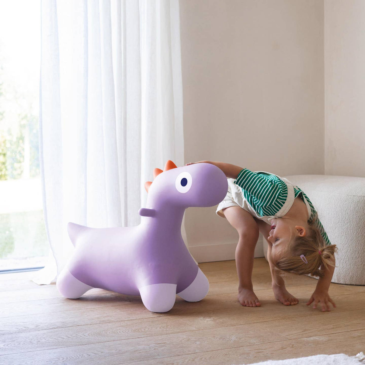 Child playing with a purple inflatable dinosaur toy indoors.