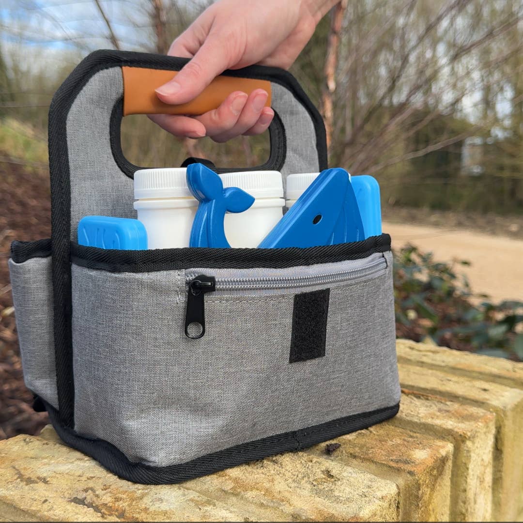 Gray cooler bag with black trim holding blue and white containers, outdoors.