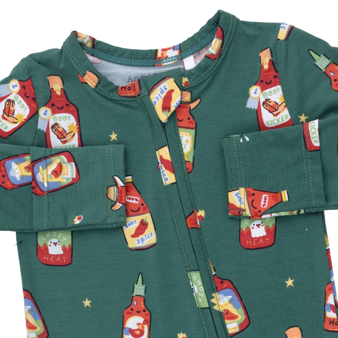 A close-up of a dark green baby romper or pajama top with a front zipper and a playful all-over print of ketchup and hot sauce bottles, stars, and small red peppers.