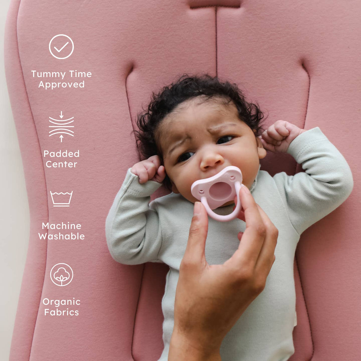 Baby lying on a pink cushion with a pacifier, surrounded by text icons indicating features.