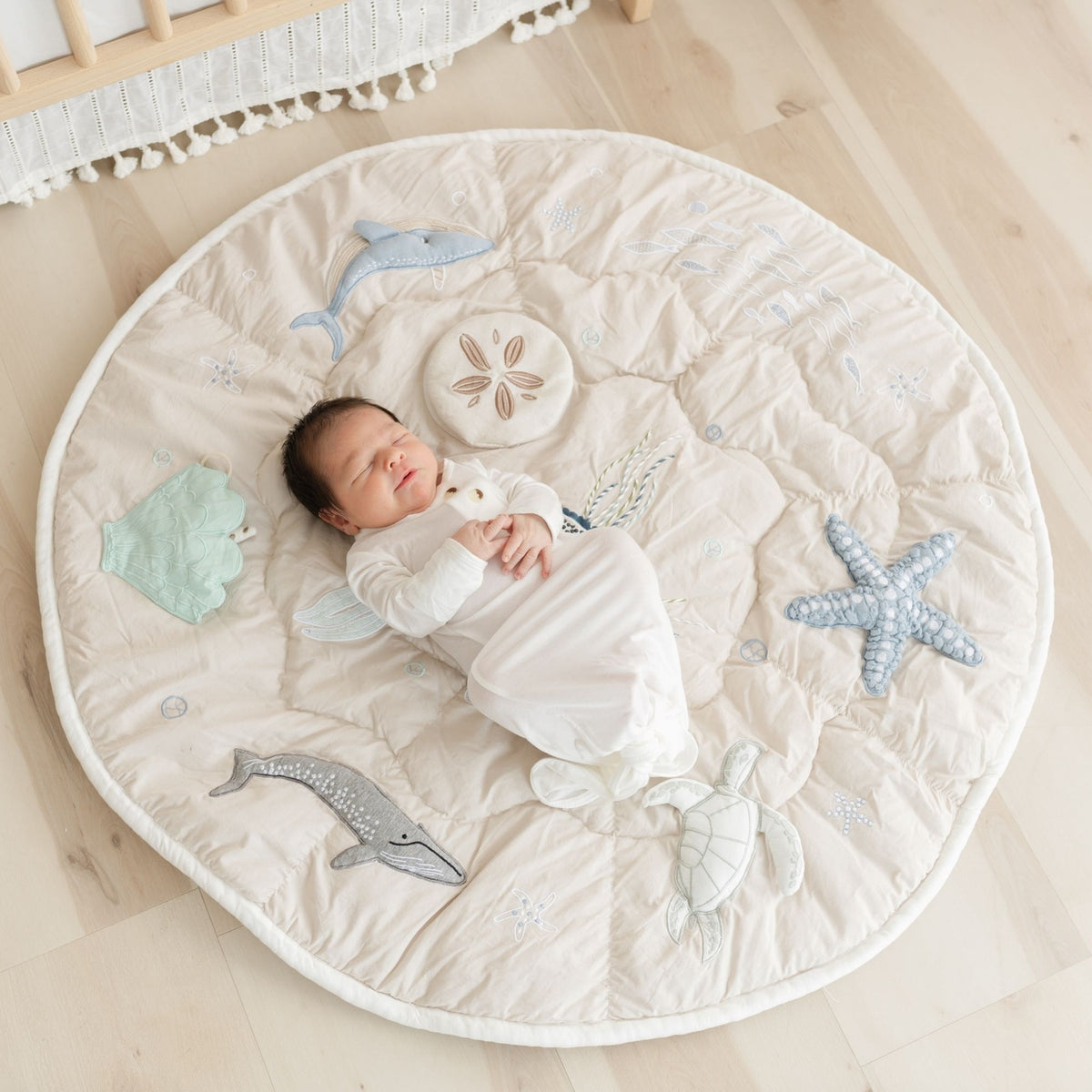 Newborn baby lying on a round play mat with sea-themed designs on a wooden floor.