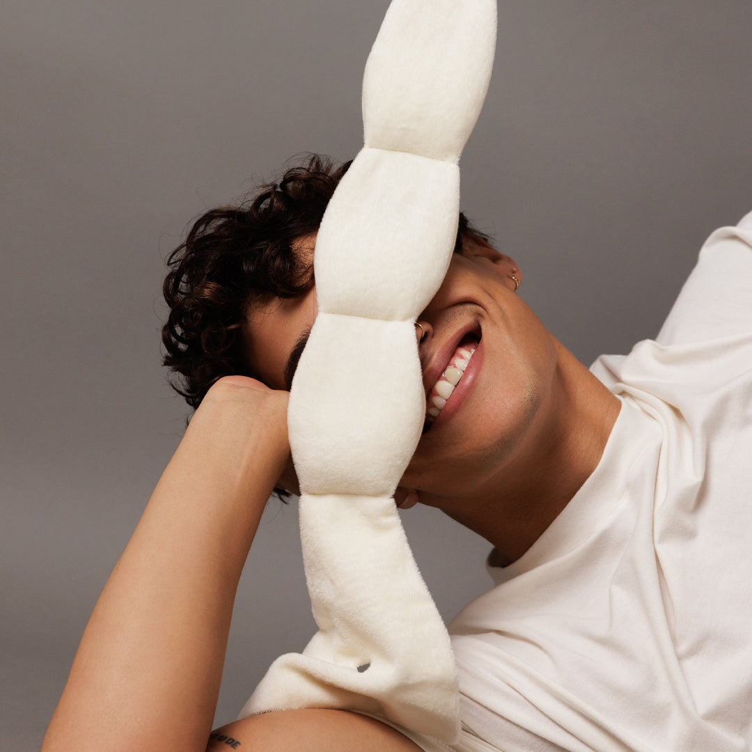 Person holding a large white foam noodle against their face on a gray background