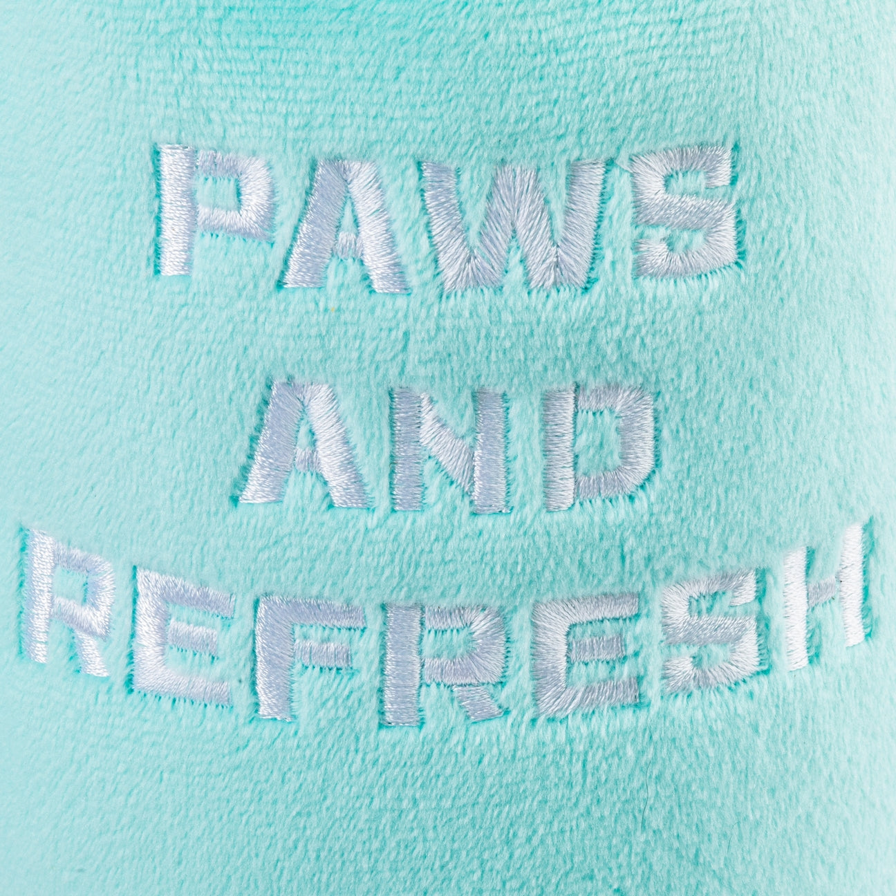 A close-up of a mint green plush fabric with white embroidered text reading 'PAWS AND REFRESH'.