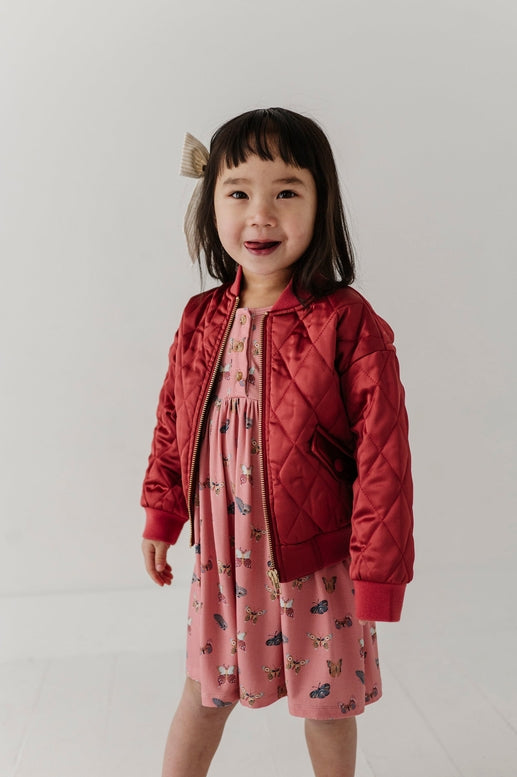 Child wearing a red jacket over a pink dress with a white background