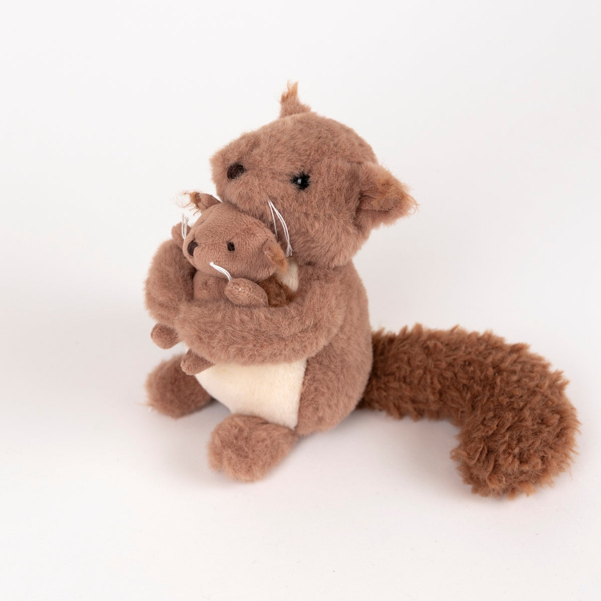 A brown plush squirrel toy holding a smaller matching squirrel, photographed on a clean white studio background.