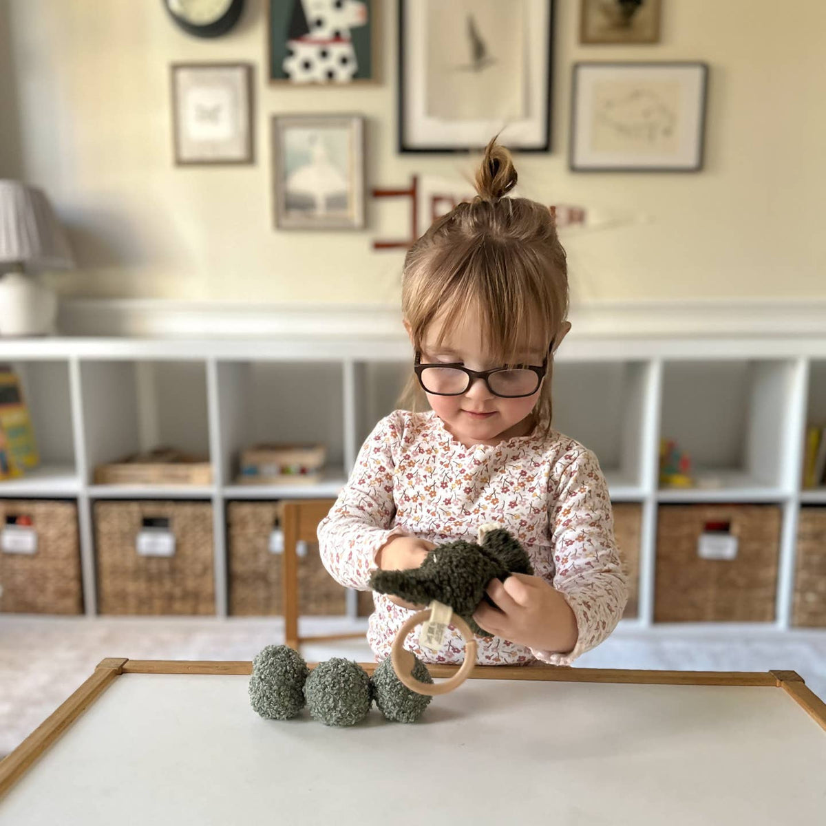 Child playing with toys in a room with shelves and framed pictures on the wall.
