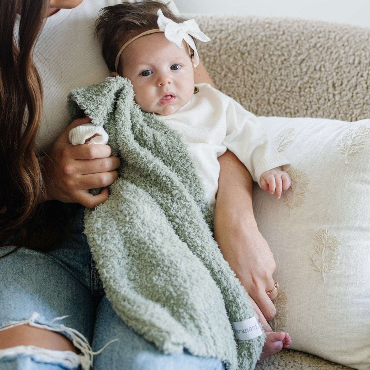 Baby wrapped in a green towel being held by a person on a couch.