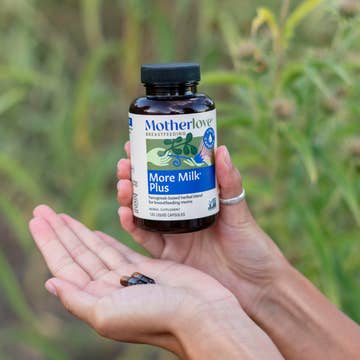 Hand holding a bottle of Motherlove More Milk Plus supplement against a natural background