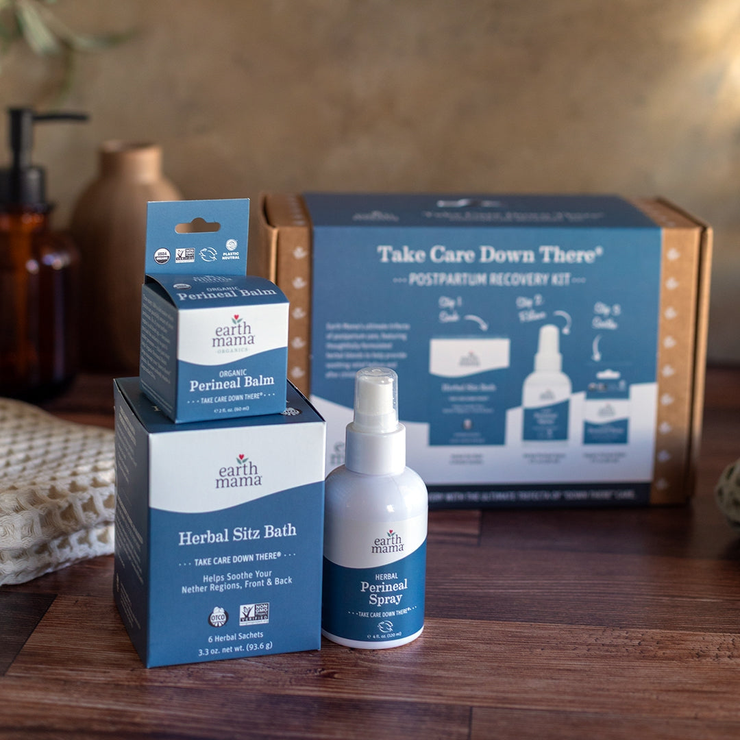 Earth Mama postpartum recovery kit with balm, sitz bath, and spray on a wooden surface.