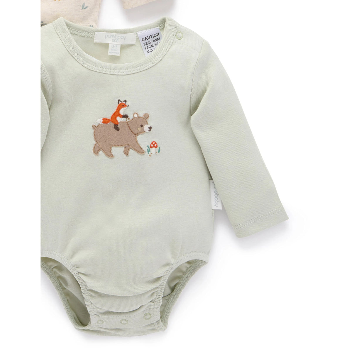 A pale sage green long-sleeve baby bodysuit featuring an embroidered design of a brown bear carrying an orange fox on its back, with a small mushroom, on a white background.