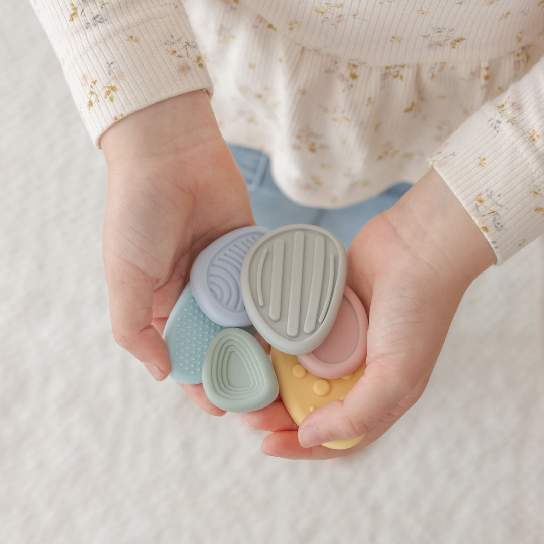 Hands holding four small, colorful objects against a neutral background