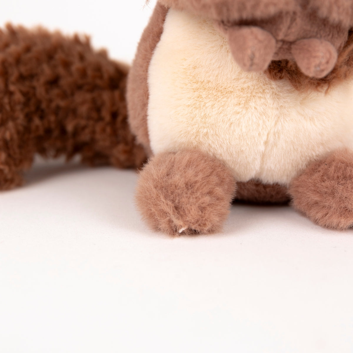 Close-up of a plush toy with brown and cream fur, showing the body and front paws on a plain white background.
