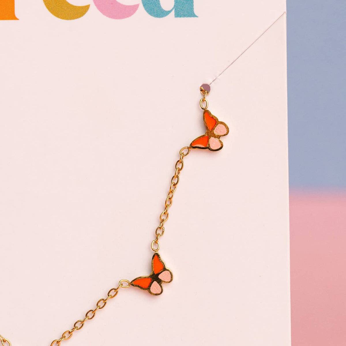 Butterfly-shaped earrings on a gold chain against a colorful background