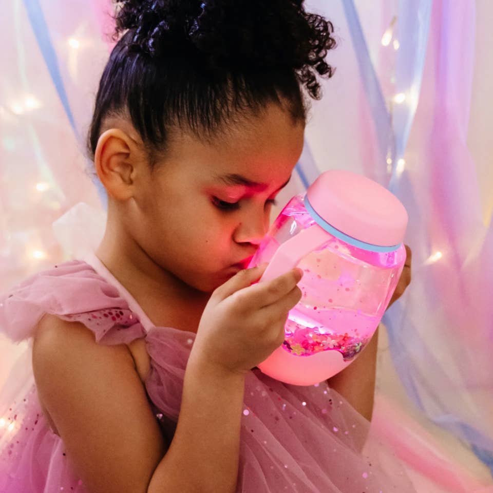 Child in a pink dress holding a pink light-up toy with a soft, blurred background