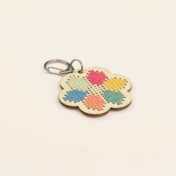 Flower-shaped keychain with colorful embroidered design on a beige background