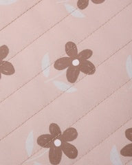 A close-up of a light pink fabric with a repeating pattern of brown flowers and white crescent shapes.
