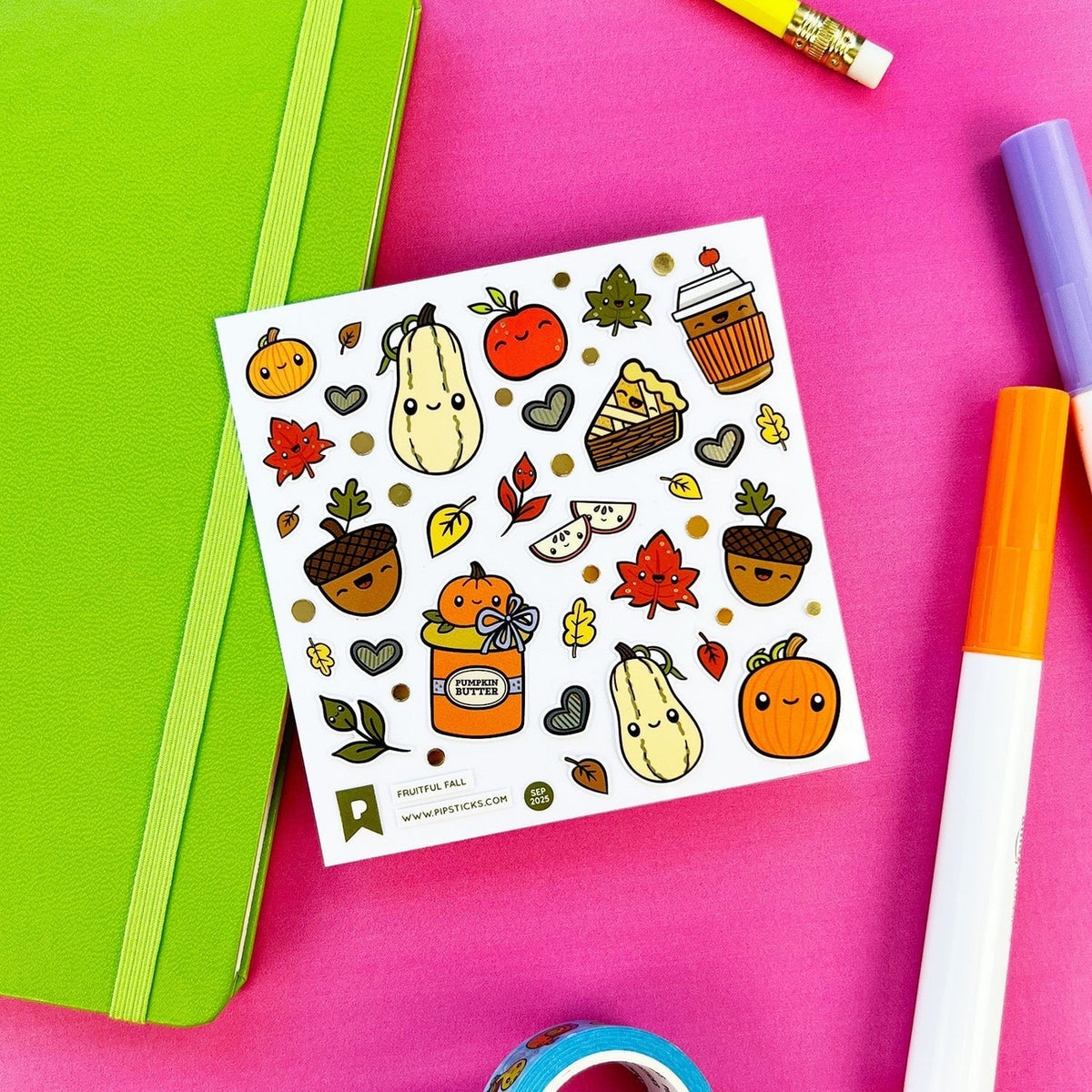 A sheet of cute autumn-themed stickers displayed on a bright pink background with a green notebook, markers, and a pencil as props. The stickers feature smiling pumpkins, acorns, leaves, and coffee cups in warm fall colors.