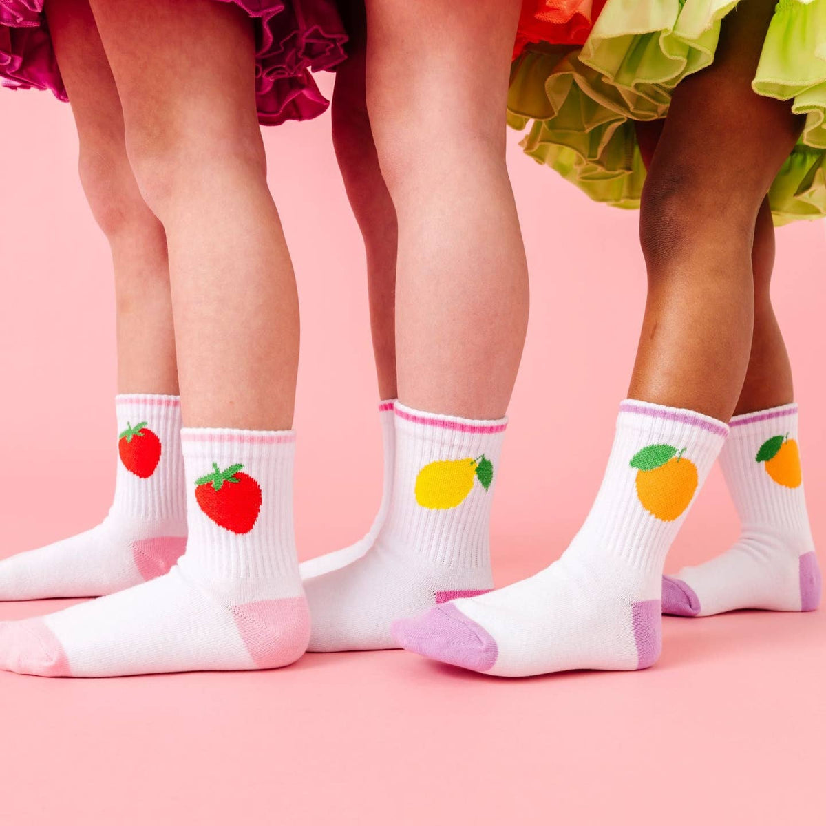 Children's legs wearing socks with fruit designs on a pink background