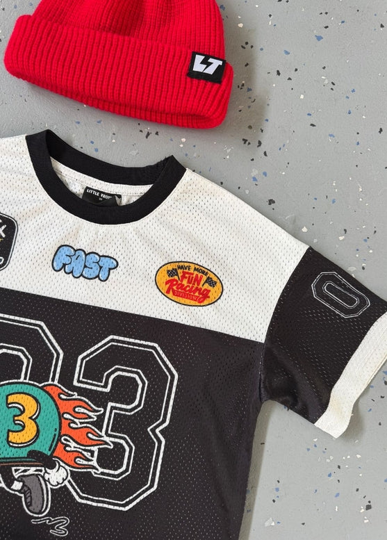 White and black sports jersey with colorful graphics and a red beanie with a logo on a gray surface.