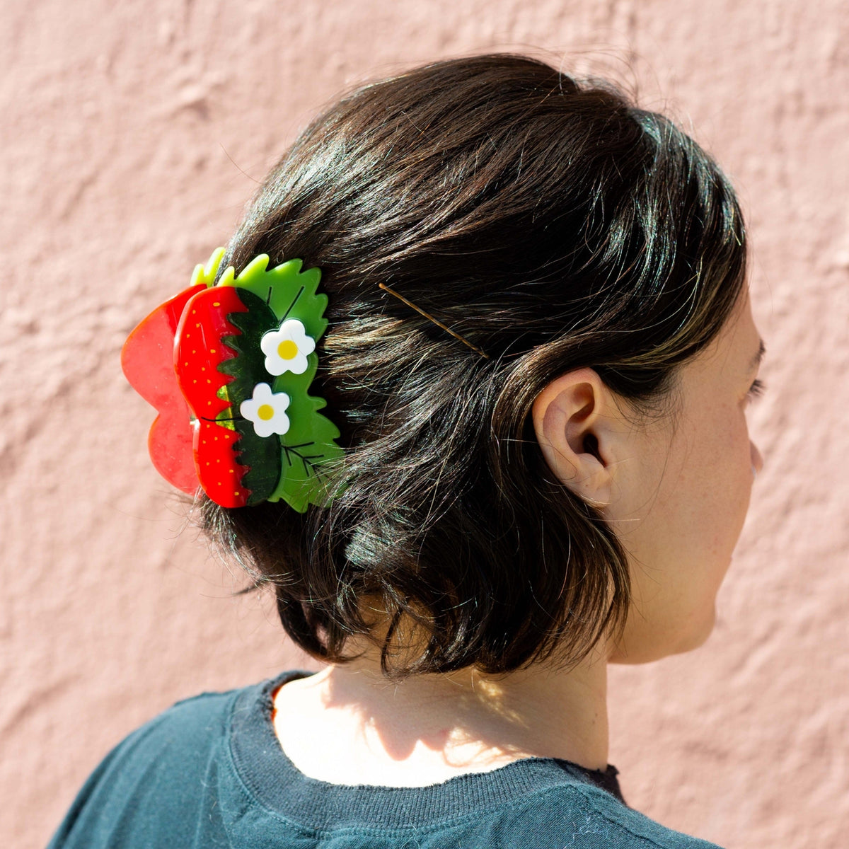 Person with a decorative hair clip resembling strawberries and flowers against a pink background