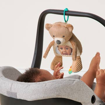 Baby in a bouncer with a teddy bear toy featuring a baby's face.