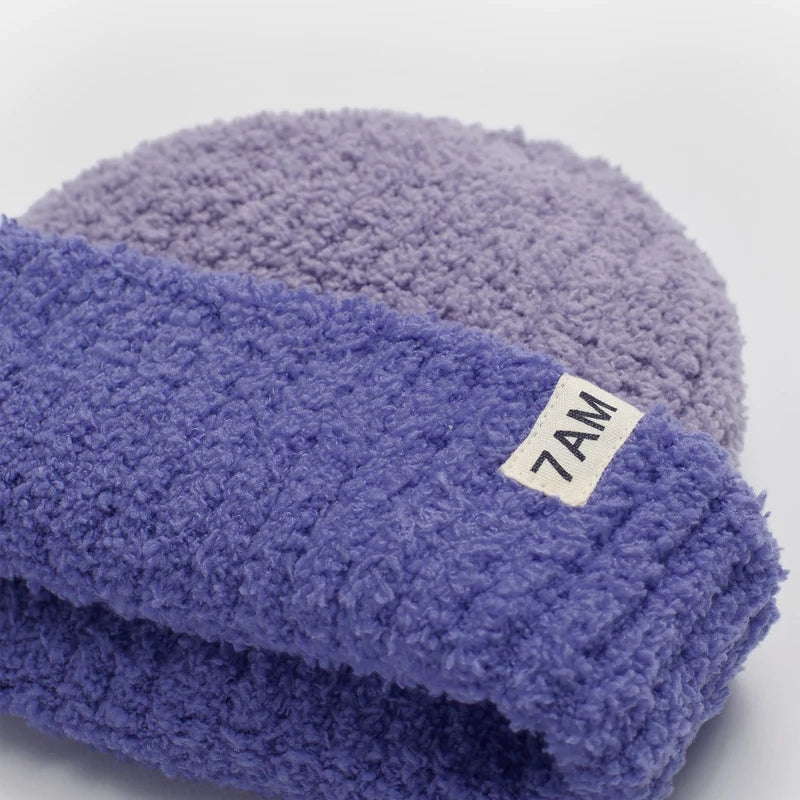 A two-tone ribbed fuzzy beanie in shades of purple (taro), featuring a folded brim with a small white tag branded with "7AM".