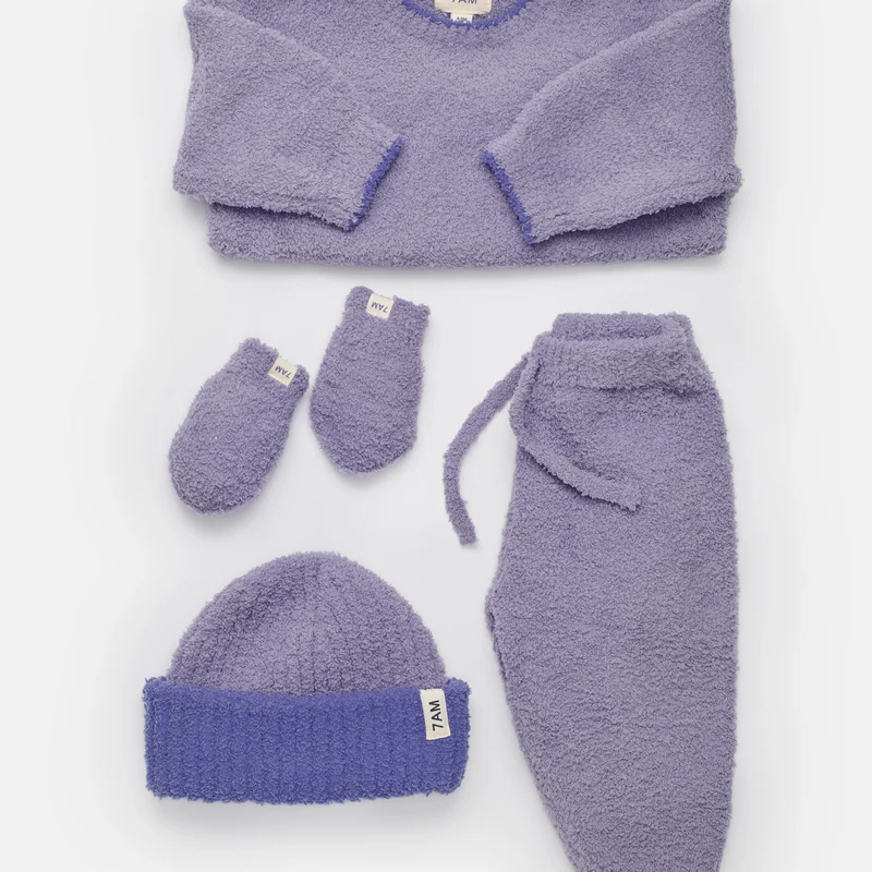 A matching purple fuzzy winter set arranged on a white background, including a boxy knit sweater, pull-on pants with a drawstring, a folded-brim ribbed beanie with a small white "7AM" tag, and a pair of mittens with matching tags.