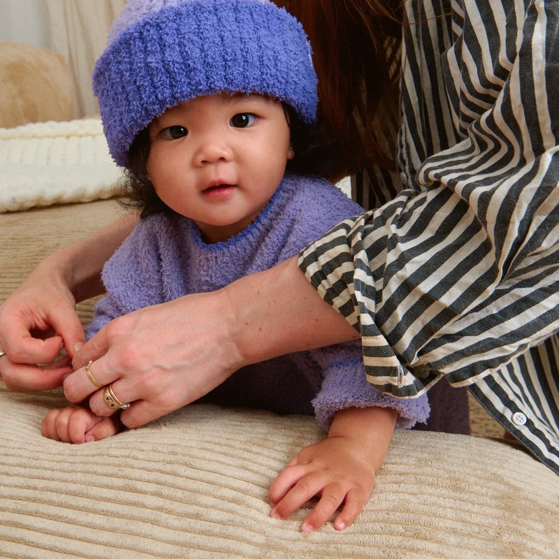 A toddler wearing a matching fuzzy purple knit sweater and a ribbed beanie with a folded brim and a white "7AM" tag.